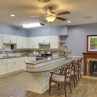 A spacious kitchen with white cabinets, a central island, wooden chairs, and a ceiling fan.
