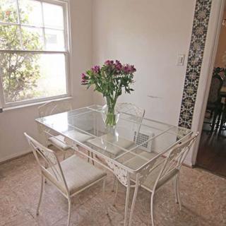 A cozy dining area with a glass table and chairs, adorned with a vase of flowers by a sunlit window.