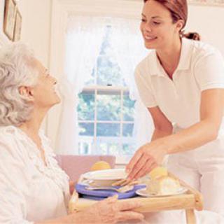 A caregiver assists an elderly woman with her meal in a comfortable home setting.