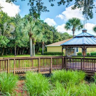 A serene garden featuring a wooden gazebo and bridge surrounded by lush greenery and trees.