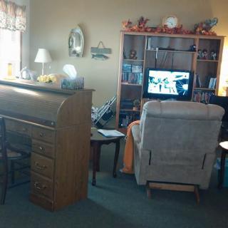 A cozy living room with a desk and bookshelf, featuring a television and a comfortable chair.
