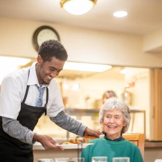 A waiter serves a smiling elderly woman at a restaurant.