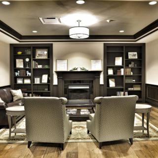 A modern living room interior featuring a cozy seating area with armchairs, a central fireplace, and bookshelves on either side.