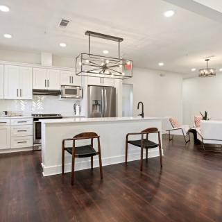 A modern kitchen with white cabinets, stainless steel appliances, and an open concept design featuring hardwood floors and an island counter with wooden chairs.