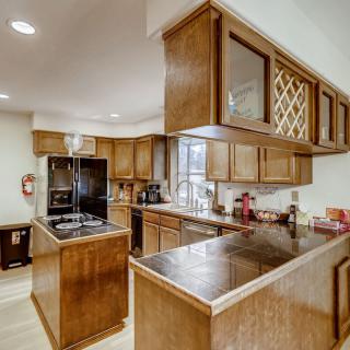 A modern kitchen with wood cabinets and an island, featuring various appliances and a countertop workspace.