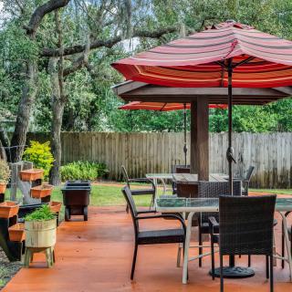 A cozy backyard patio with tables and chairs under umbrellas, surrounded by trees and a wooden fence.
