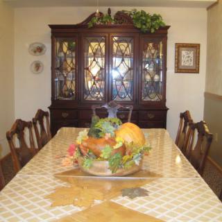 A dining room with a long table and chairs, featuring a decorative centerpiece, with an elegant cabinet in the background.
