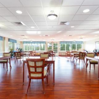 A spacious and bright dining room with wooden floors, neatly arranged tables, and chairs.