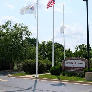 An entrance with flags and a sign, surrounded by trees on a sunny day.