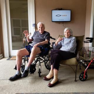 An elderly couple enjoying a sunny day together, greeting the camera with smiles.