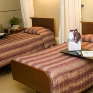 A hospital room with two beds featuring striped bedding, separated by curtains. A tray is placed on one bed.