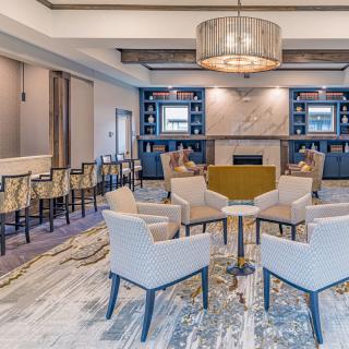 A modern lounge area featuring comfortable seating around a fireplace, accompanied by bookshelves and a stylish chandelier.