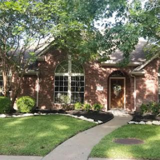 A charming brick house surrounded by lush greenery and a welcoming pathway.