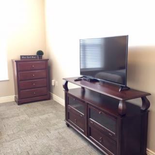 A cozy living room setup with a TV on a wooden stand and a dresser against the wall.