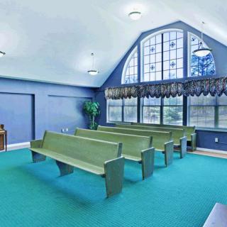 A chapel interior with green pews, large windows, and teal carpet.