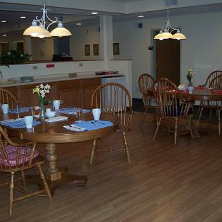 A neatly set dining room with wooden tables and chairs, illuminated by overhead lamps.