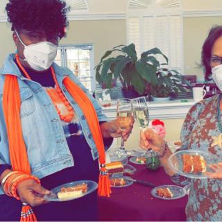 Two people wearing masks enjoy cake and drinks at a festive indoor gathering.