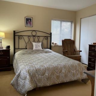 A cozy bedroom with a neatly made bed, a lamp on a nightstand, a rocking chair, and a dresser.