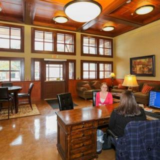 A welcoming office reception area with a wooden ceiling, featuring a desk where two people are seated and a cozy lounge space in the background.
