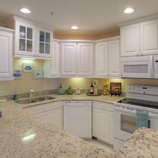 A modern kitchen with white cabinets and granite countertops, featuring built-in appliances and well-lit spaces.