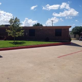 A sunny day view of a brick building with a landscaped parking area.