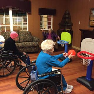 Elderly individuals in wheelchairs playing basketball indoors.
