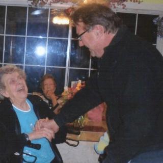 An elderly woman shares a joyful moment with a man indoors.