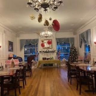 A festive dining room adorned with Christmas decorations, featuring elegant chandeliers and neatly arranged tables and chairs.