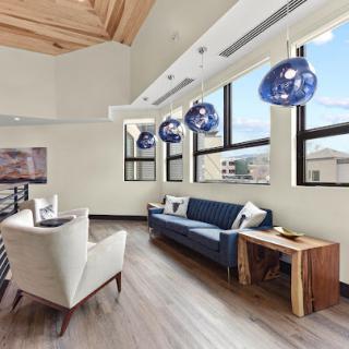 A modern living room featuring stylish blue pendant lights, a comfortable sofa, and large windows allowing ample natural light.