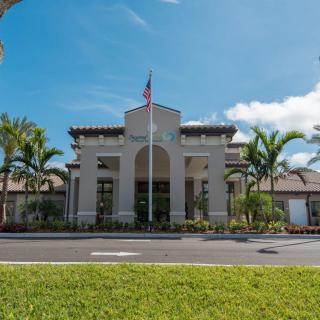 A large building with palm trees and a flag in front, set against a clear blue sky.
