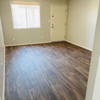An empty room with hardwood flooring, featuring a window and a door.