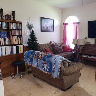 A cozy living room with a sofa, bookshelf, TV, and piano.