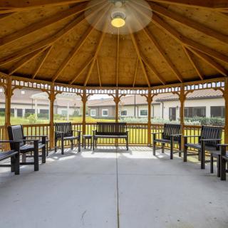A wooden gazebo with benches arranged in a circle, situated in a landscaped area.
