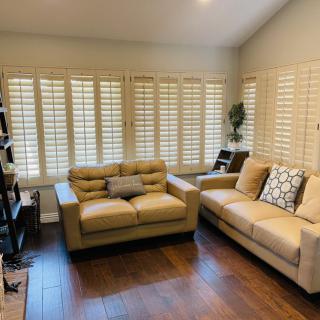 A cozy living room with two beige sofas, wooden floors, and window shutters.