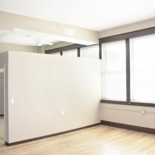 An empty apartment with large windows and hardwood flooring.