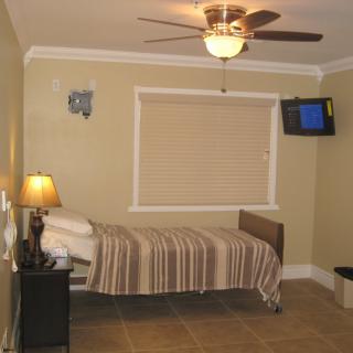 A small bedroom with a single bed, ceiling fan, wall-mounted television, and a lamp on a nightstand.