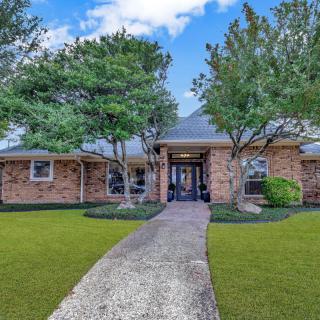 A brick house with a well-maintained lawn and trees lining the pathway.