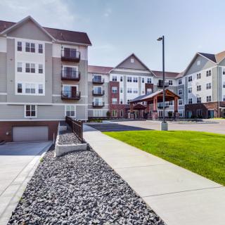 A modern residential apartment complex with well-maintained landscaping and a paved pathway.
