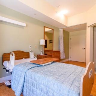 A well-equipped hospital room featuring a patient bed with a table, lamp, and mirror.