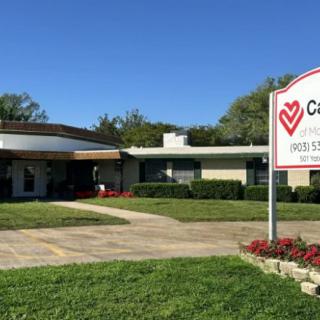 A care facility building with a sign and well-maintained lawn under a clear blue sky.