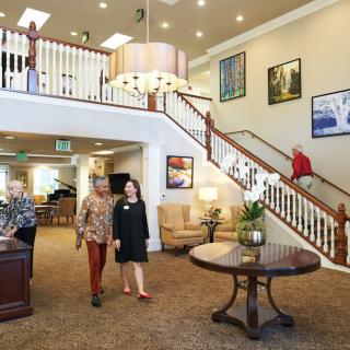 A spacious lobby with a grand staircase, multiple people walking and seated, and elegant decor.