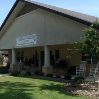 A building with a porch featuring rocking chairs and a sign, surrounded by landscaping and a lawn.