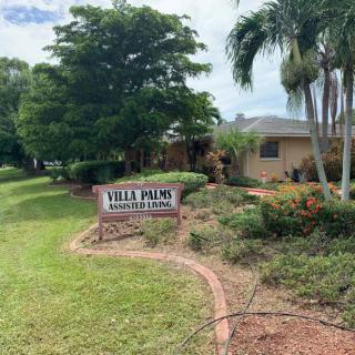 A view of a building surrounded by lush landscaping and palm trees, featuring a sign labeled 'Villa Palms'.