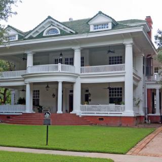 A historic colonial-style house with a large porch and manicured lawn.