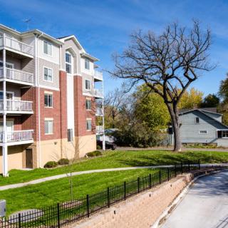 A residential apartment building with a neatly maintained lawn and pathway under a clear blue sky.