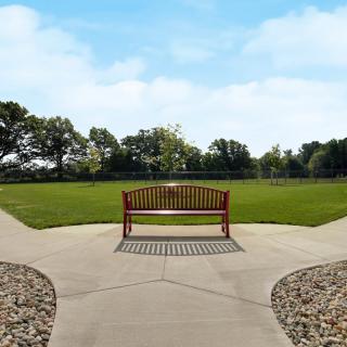 A wooden bench situated at the intersection of two pathways in a park with green grass and trees.