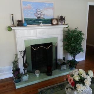 A cozy living room with a decorated fireplace and mantel, featuring artwork, a clock, and a floral arrangement.
