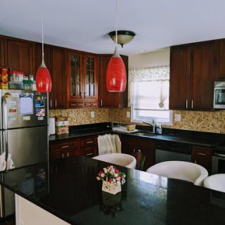 A stylish modern kitchen featuring dark wooden cabinetry, sleek granite countertops, and vibrant red pendant lights.