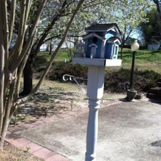 A charming blue birdhouse set on a white post in a serene garden.