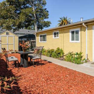 A cozy backyard with outdoor seating and landscaping around a yellow house on a sunny day.